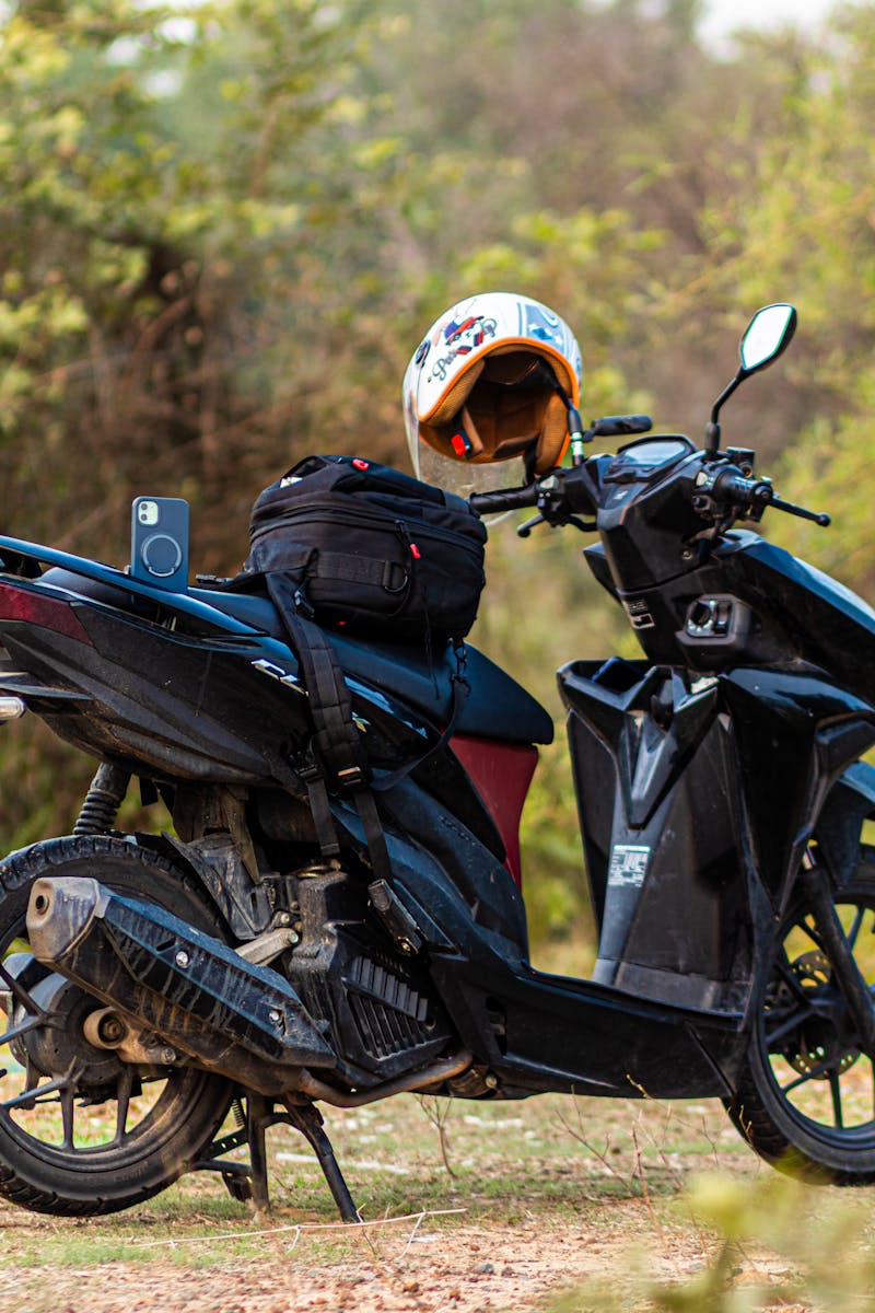 A motorcycle with a helmet and backpack parked outdoors in Cambodia, surrounded by greenery.