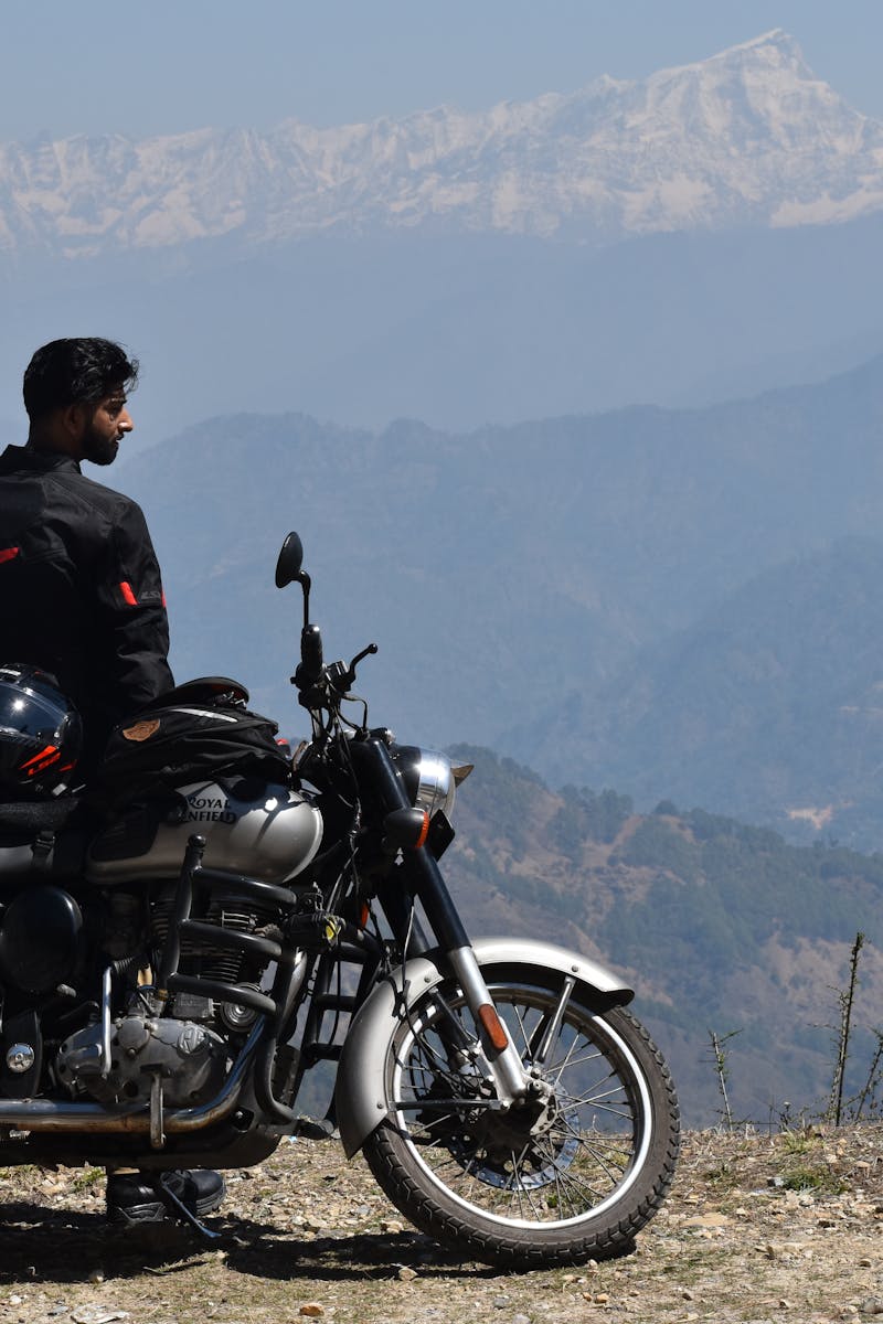 A motorcyclist with a Royal Enfield on a mountain road in Pithoragarh, Uttarakhand, enjoying the Himalayan view.
