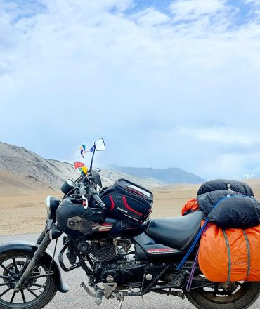 Motorcycle parked in barren desert landscape near Pang under a blue sky.
