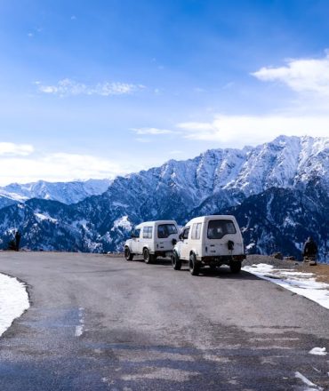 Idyllic winter road trip scene with vehicles and mountains in Himachal Pradesh.