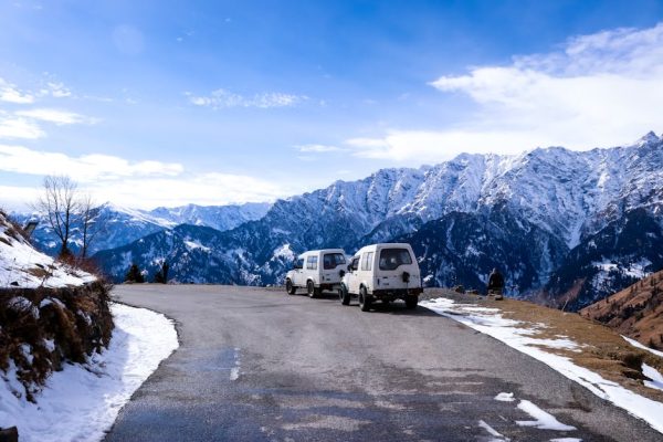 Idyllic winter road trip scene with vehicles and mountains in Himachal Pradesh.